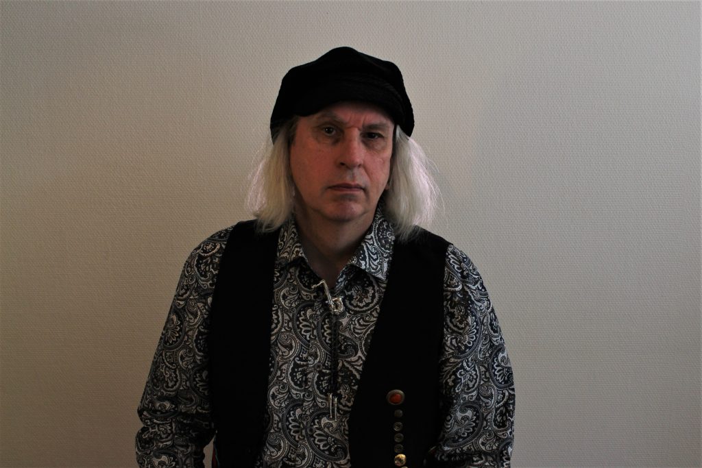 Petri Vanninen, artistinimeltään Kelja, poseeraa kameralle vaalean seinän edessä.